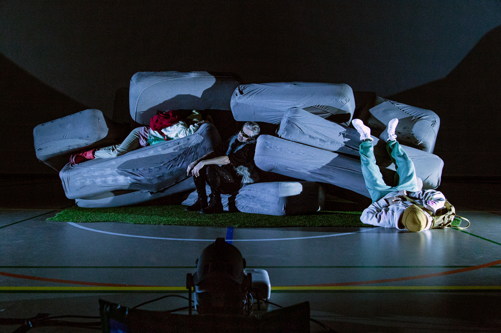 Kolme näyttelijää patjojen seassa näyttämöllä.