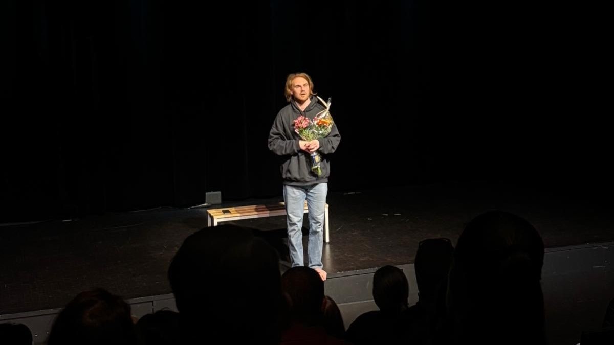 Miesnäyttelijä lavalla kukkakimppu sylissään.